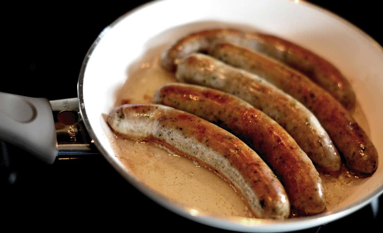 Polish sausages sizzling in a frying pan on a stove.