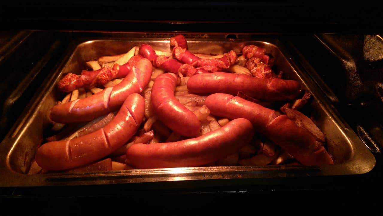 A tray of traditional Polish sausages and crispy potatoes baking in the oven.