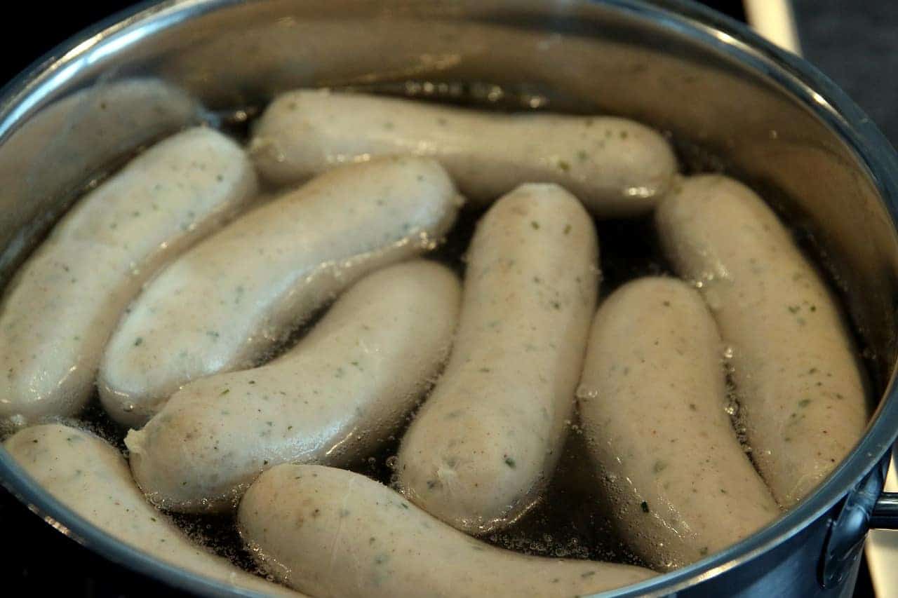 Polish sausages sizzling in a pot on a stove.