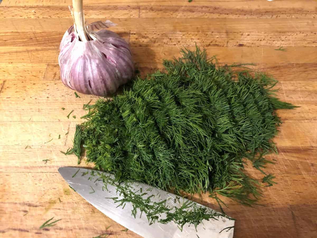 A knife and a bunch of dill on a cutting board, accompanied by Sos Koperkowy Dill Sauce.