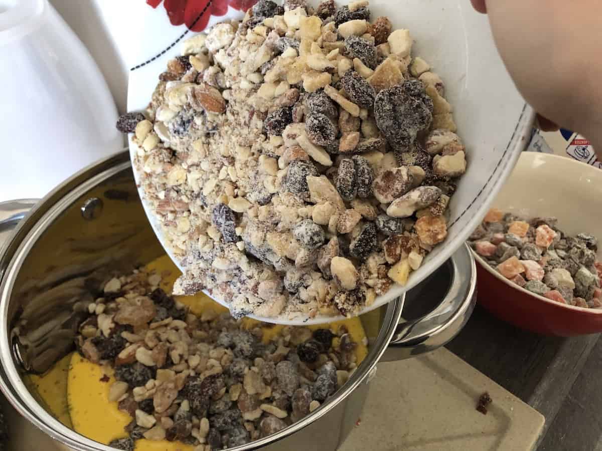 A person preparing a Polish fruitcake recipe by pouring granola into a bowl.