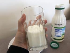 A person holding a glass of milk next to a bottle, pondering what to serve with perogies.