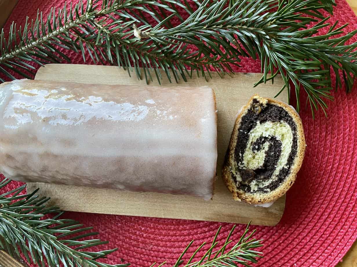 A poppyseed roll is sitting on a cutting board next to a pine branch, alongside a poppy seed roll.