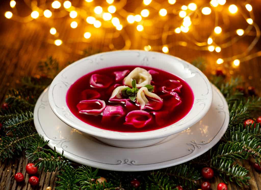 A traditional Polish beet soup, known as uszka, is beautifully presented in a rustic wooden bowl on a table.