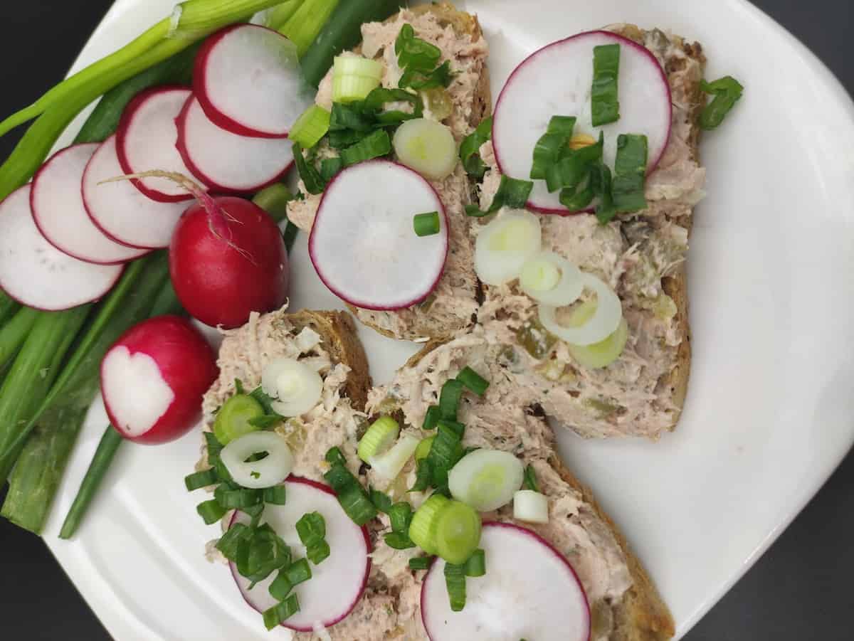 A platter of chicken spread on bread with radishes and leeks.