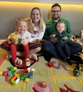 A family sits on a rug with toys in front of them while enjoying recipes from the Polish Easter Cookbook.