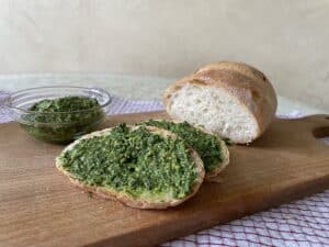 Vegan bread topped with pesto and fresh parsley on a wooden cutting board.