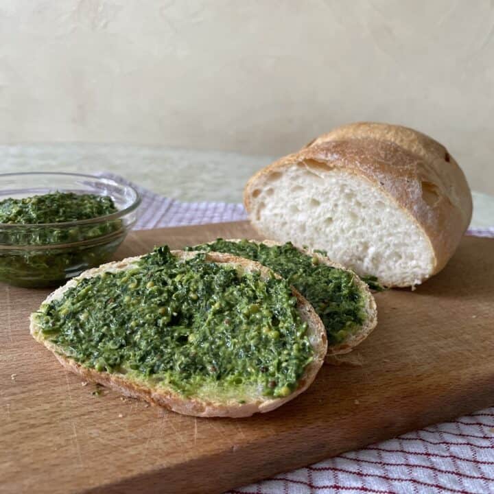 Vegan bread topped with pesto and fresh parsley on a wooden cutting board.