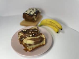 A slice of vegan banana bread on a plate next to a banana.