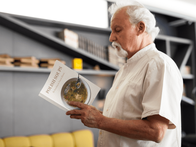 An older man reading a Polish cookbook in a living room.