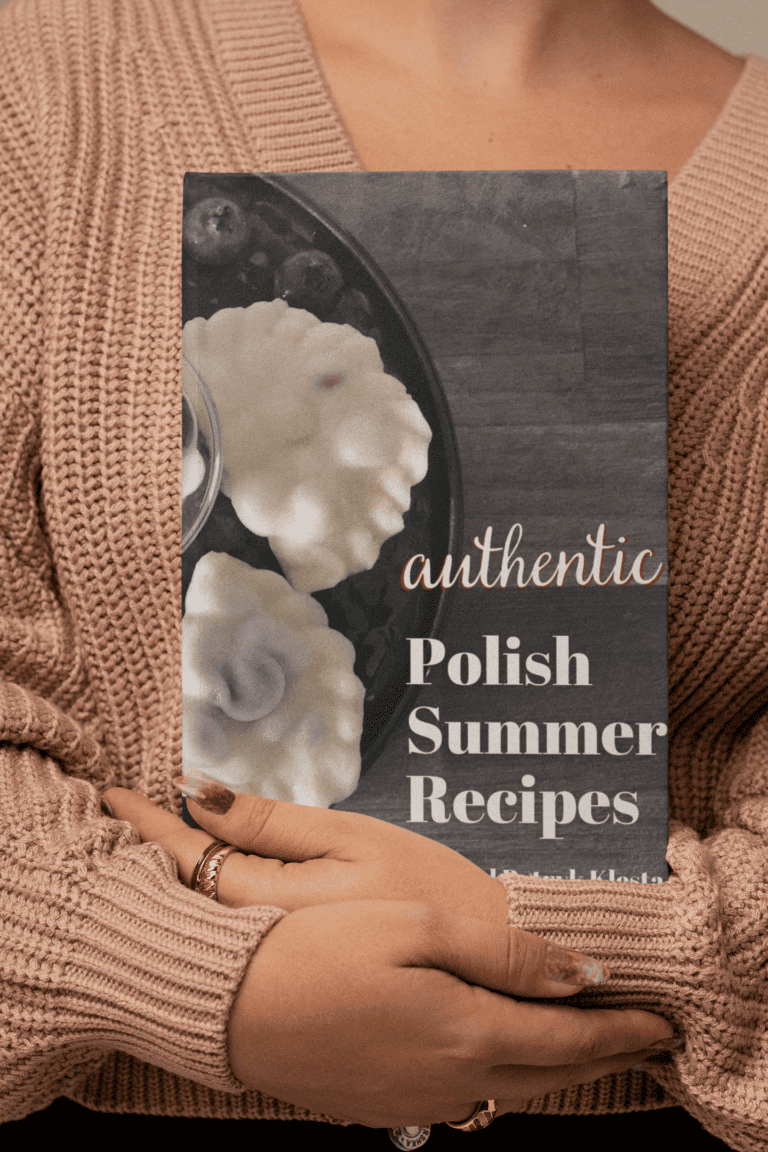 A person wearing a beige knit sweater is holding a cookbook titled "Polish Summer Recipes" with an image of traditional pastries on the cover.