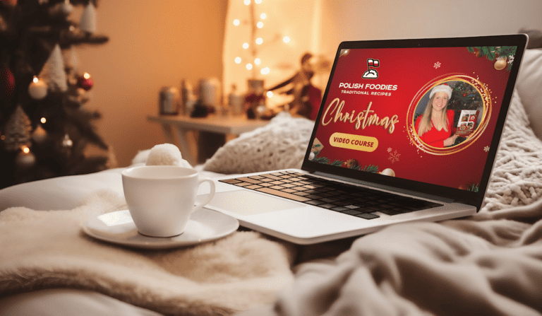 A laptop on a bed displays a Polish Christmas video course called "Polish Foodies Traditional Recipes." A cup of coffee sits next to the laptop in a cozy, festive room.