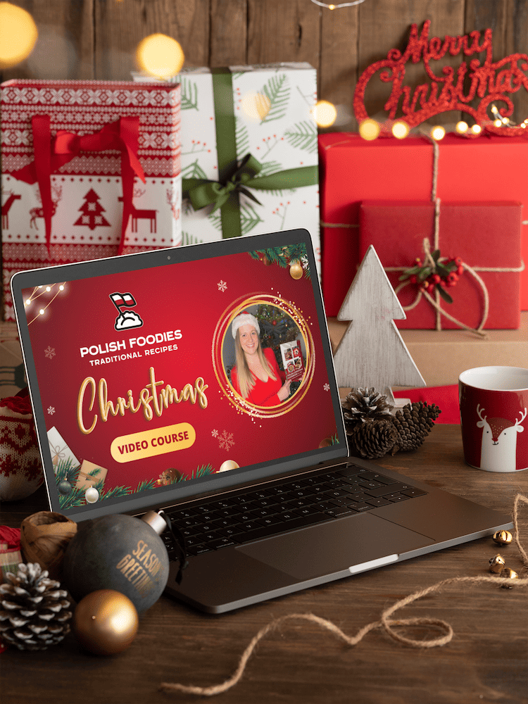 A laptop displaying a "Polish Foodies Christmas Video Course" page sits on a wooden table surrounded by Christmas gifts, decorations, a ceramic mug, a small tree, and a pinecone, capturing the essence of a traditional Polish Christmas.