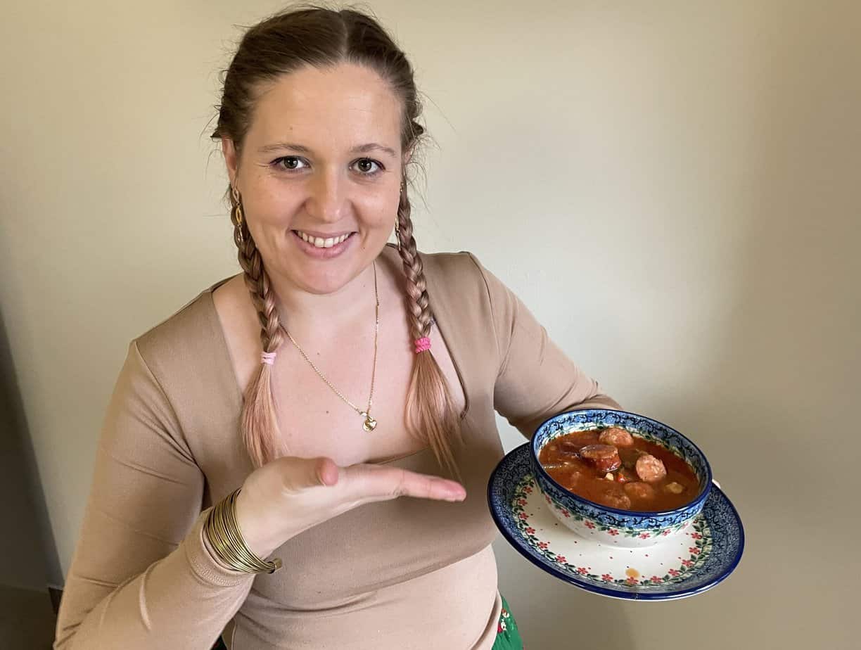 A Polish woman holding up a bowl of meat stew, following a traditional recipe.