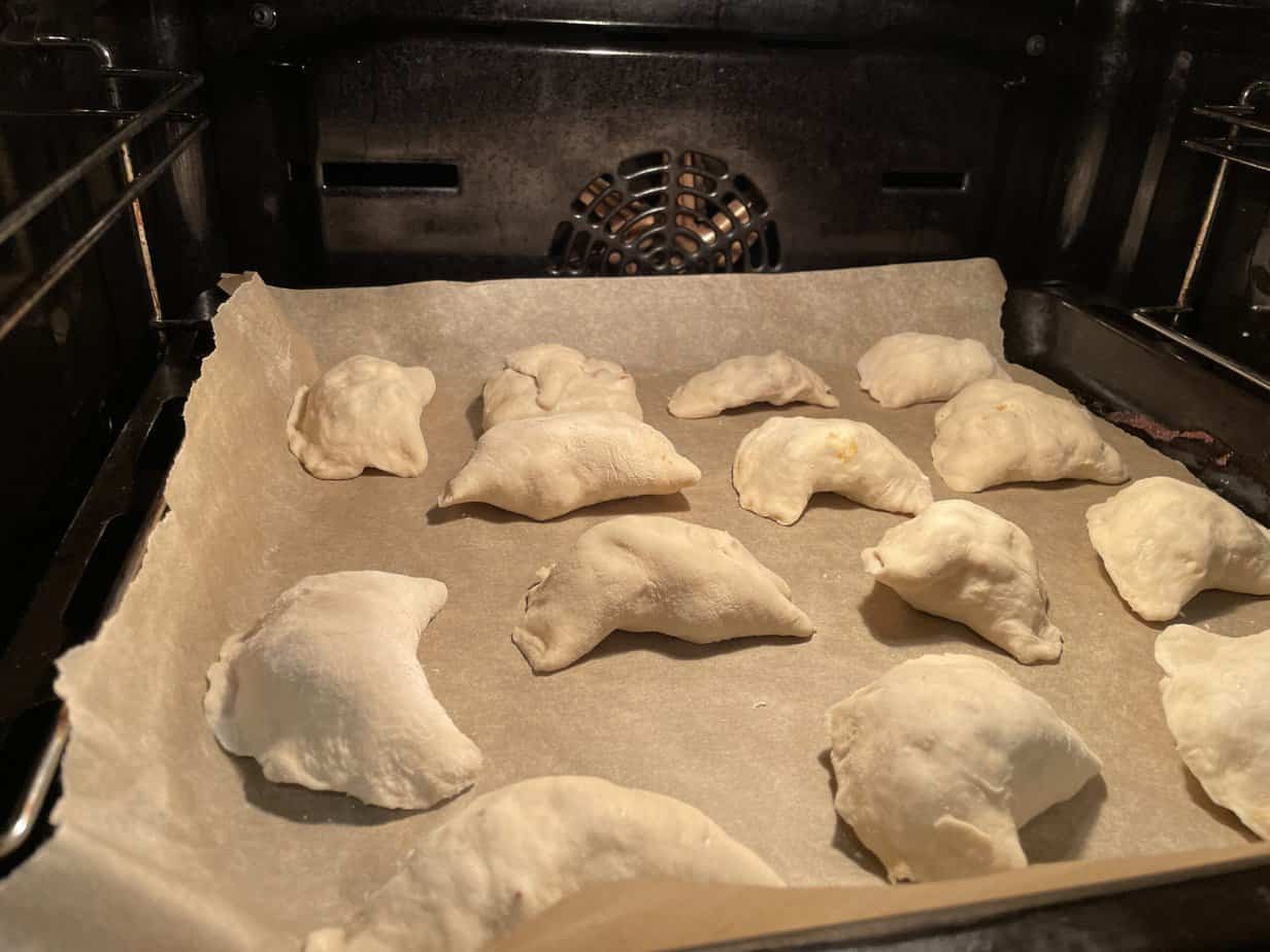 Bake unbaked pierogi pockets on a parchment-lined baking tray inside an oven.