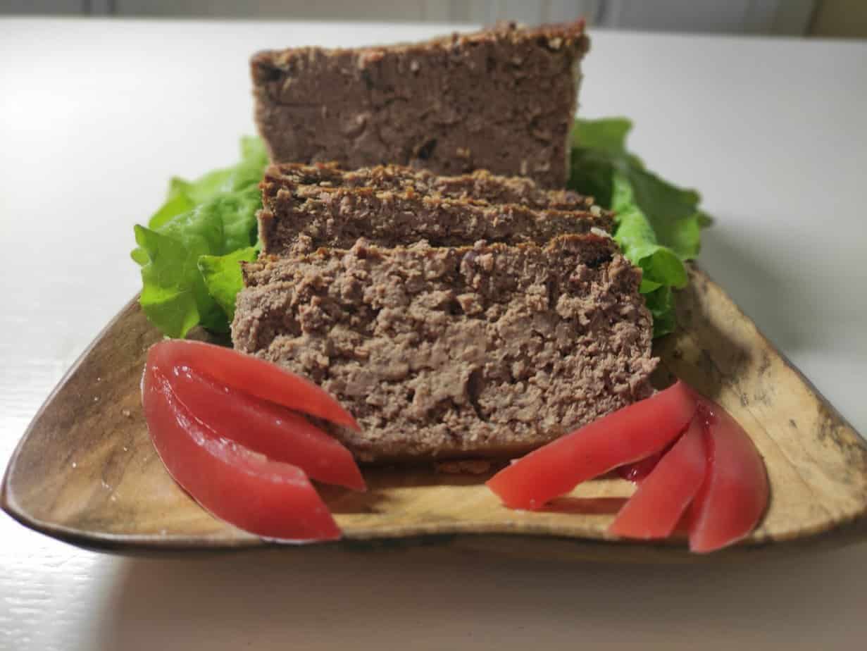 Slices of chicken meatloaf on a lettuce bed with tomato wedges on a wooden plate.