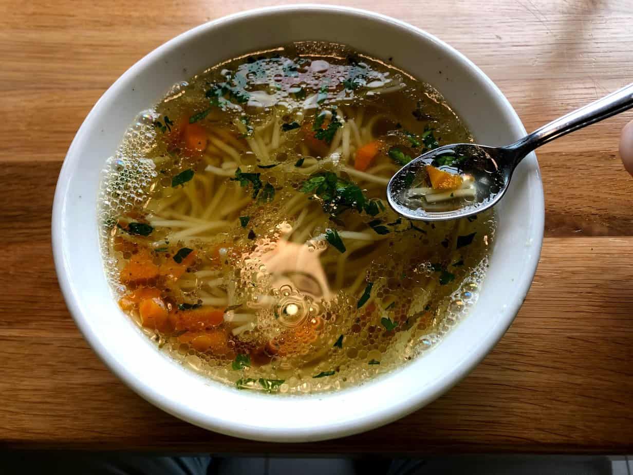 A bowl of top Polish chicken noodle soup with carrots, parsley, and a spoon, served on a wooden table.