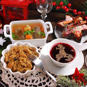 A table set with festive decorations displays a traditional Polish Christmas meal consisting of clear soup with meat and vegetables, sauerkraut dish, red beverage with herbs, and a star-shaped cake.
