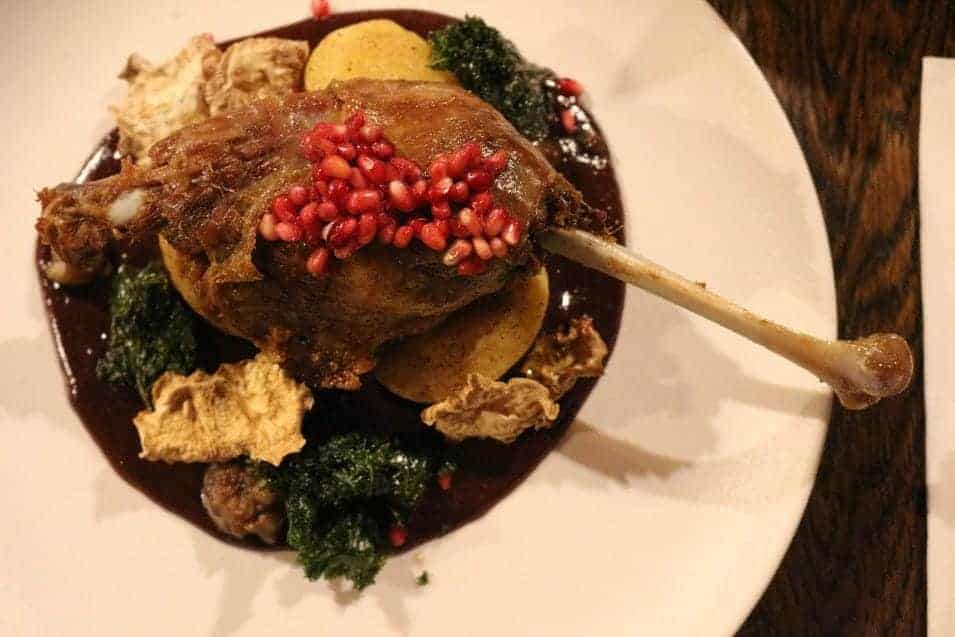 A cooked duck leg garnished with pomegranate seeds, served on a dark sauce with assorted vegetables and crisps on a white plate—a perfect choice for those exploring Wrocław restaurants and wondering where to eat Wrocław.