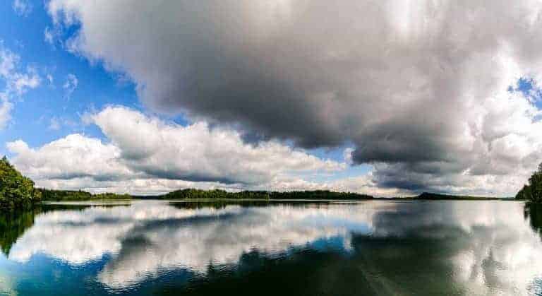 A large lake reflects dramatic clouds and a blue sky, with tree-lined shores visible in the distance—one of the beautiful places in Poland that invites you to visit Poland and enjoy its natural wonders.