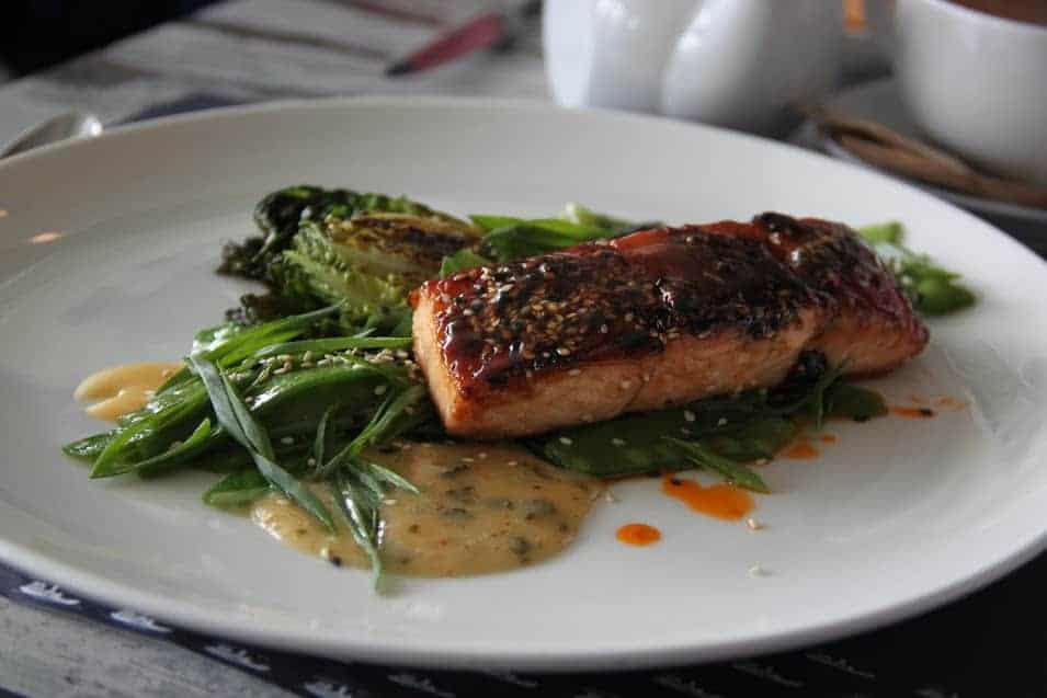 A plate with glazed salmon on a bed of green vegetables, drizzled with sauce and garnished with sesame seeds—a must-try for anyone exploring Wrocław food or searching for top restaurants Wrocław has to offer.