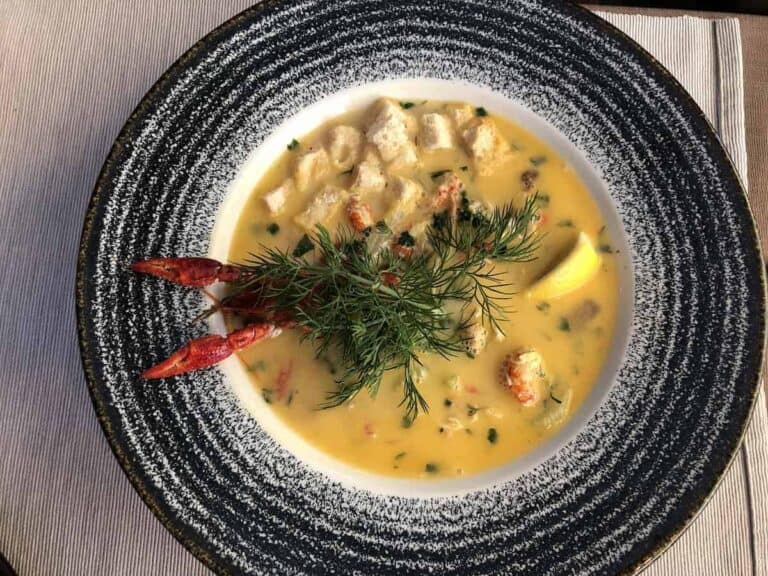 A bowl of creamy yellow seafood soup, garnished with fresh dill, croutons, lemon wedge, and crayfish claws on a speckled plate—a must-try for anyone searching where to eat authentic flavors in restaurants Wrocław offers.