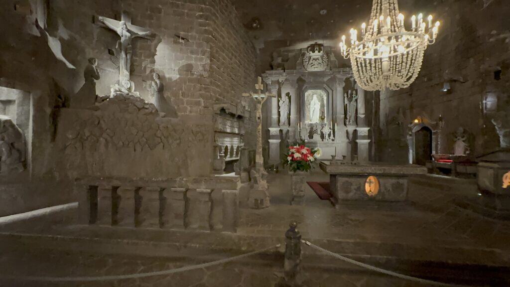 Dimly lit stone chapel interior with religious statues, an altar adorned with flowers, and a chandelier hanging from the ceiling—one of the beautiful places in Poland worth visiting.