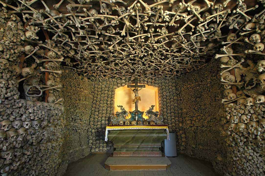 A chapel interior in Dolnośląskie, with walls and ceiling densely decorated with human skulls and bones, centered around an altar with a crucifix—one of the best places to visit for those interested in unique Poland travel experiences.