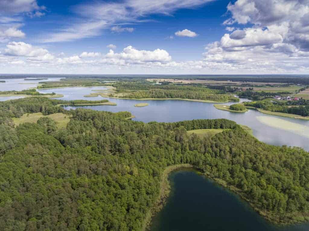 Aerial view of a landscape with dense forests, several lakes, grassy patches, and partly cloudy skies—showcasing the natural beauty found in breathtaking national parks in Poland.
