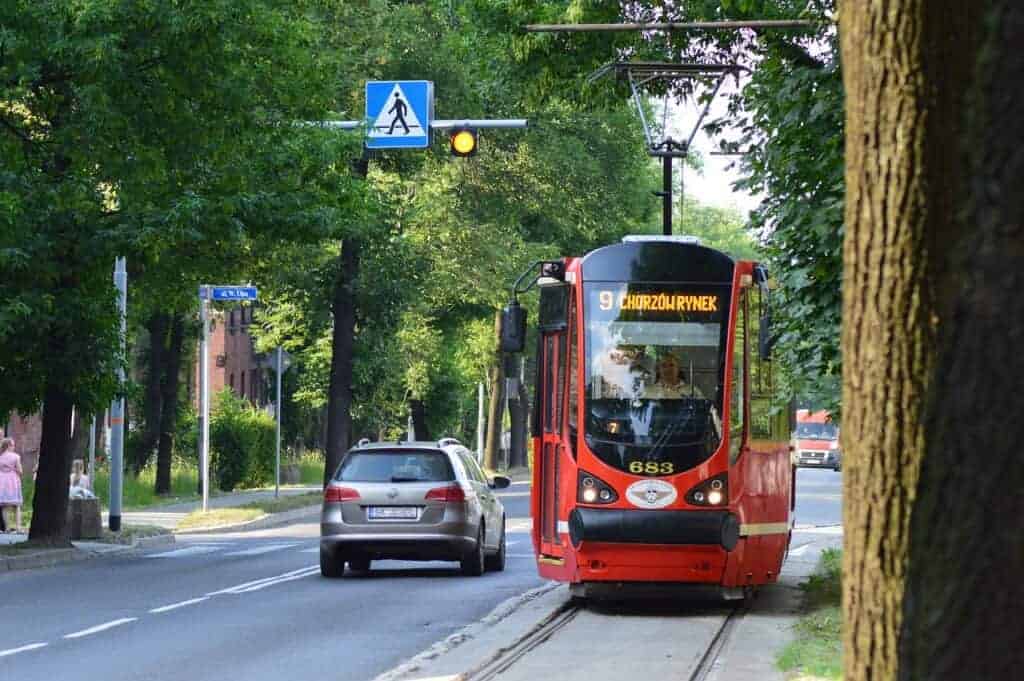 A red tram labeled "9 Chorzów Rynek" travels along tracks beside a road with a car and a pedestrian crossing sign overhead, surrounded by trees—a charming scene in Slaskie Poland, one of the Best Places Slaskie to explore.