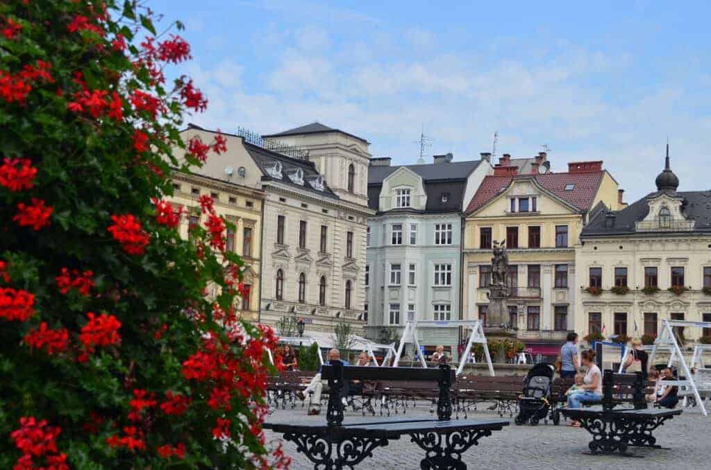 Town square with benches, people sitting, and historic buildings in the background; red flowers in the foreground on the left—one of the best places to visit when you travel through Slaskie, Poland.