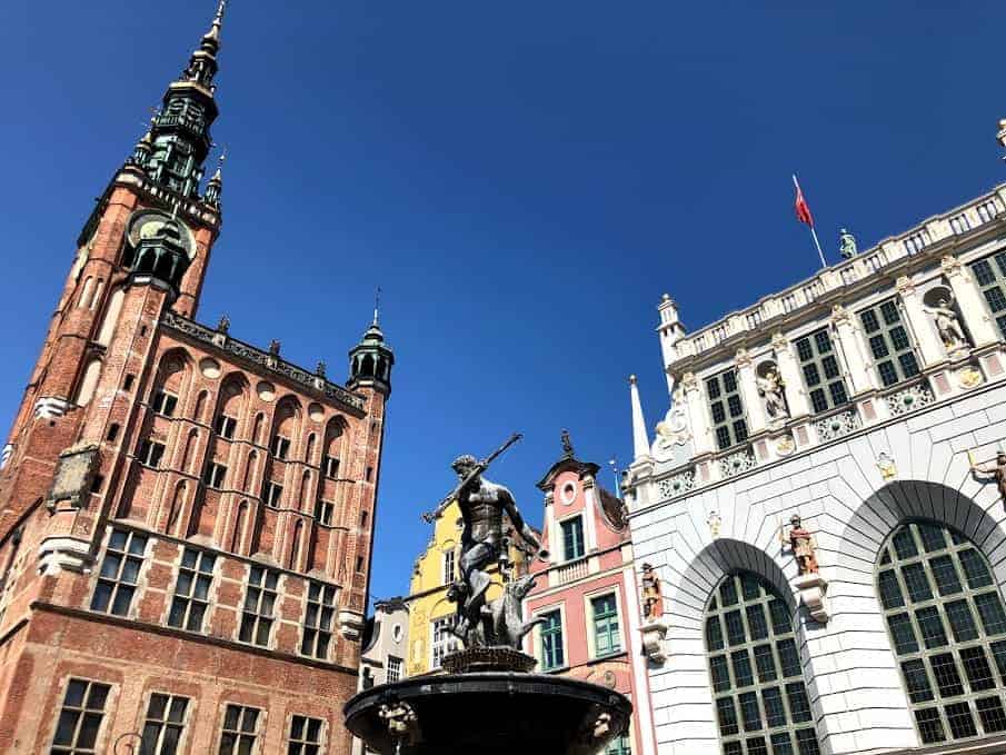 Historic buildings and a statue of Neptune under a clear blue sky in a charming Polish city square—just one of the things we love about travel in Poland.