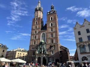 A large brick church with two tall towers and a central entrance stands in a busy square under a blue sky, surrounded by historic buildings and people—one of the top things to see in Poland on any 5 days itinerary.