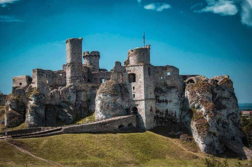 Stone ruins of a medieval castle sit atop a rocky hill under a clear blue sky—one of the best places to visit in Slaskie, Poland, as highlighted by any good travel guide.
