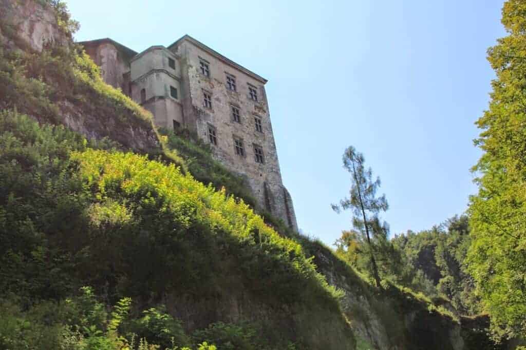 A tall, old stone building with many windows stands on a steep, grassy hillside under a clear blue sky—an iconic scene often found while exploring Poland travel gems like National Parks Poland.