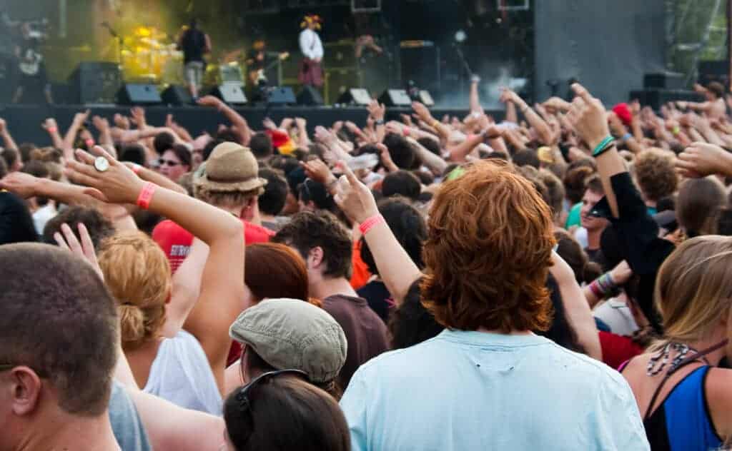 A large crowd enjoys an outdoor concert with raised hands, facing a vibrant stage and bright lights—a perfect snapshot of Summer in Poland for those visiting Poland during the lively festival season.