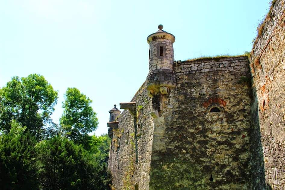 Stone fortress wall with cylindrical watchtowers, surrounded by trees and greenery under a clear blue sky—a stunning example of must-see castles in Poland.