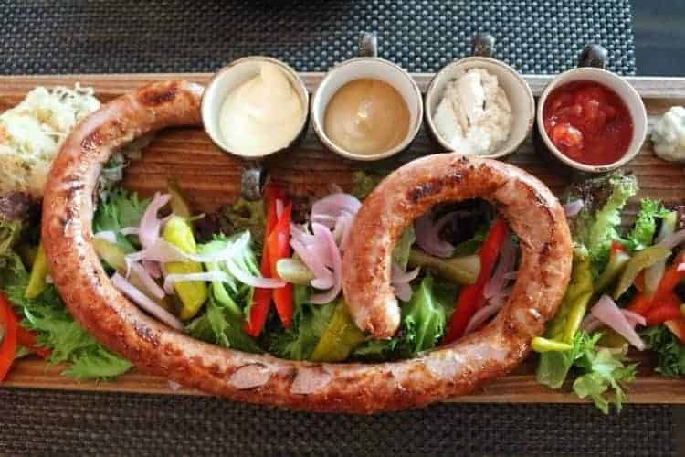 A coiled grilled sausage served on a wooden board with mixed salad, sliced vegetables, and four dipping sauces—a delicious taste of Zakopane Poland and a must-try for food lovers exploring things to do in Zakopane.