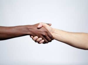 Two people of color with different skin tones shaking hands against a plain, light-colored background, subtly representing unity amid ongoing conversations about racism in Poland.
