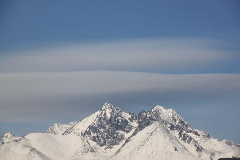 Snow-covered mountain peaks under a blue sky with layered, elongated clouds above—a stunning view that showcases the off the beaten path beauty of Zakopane, Poland.