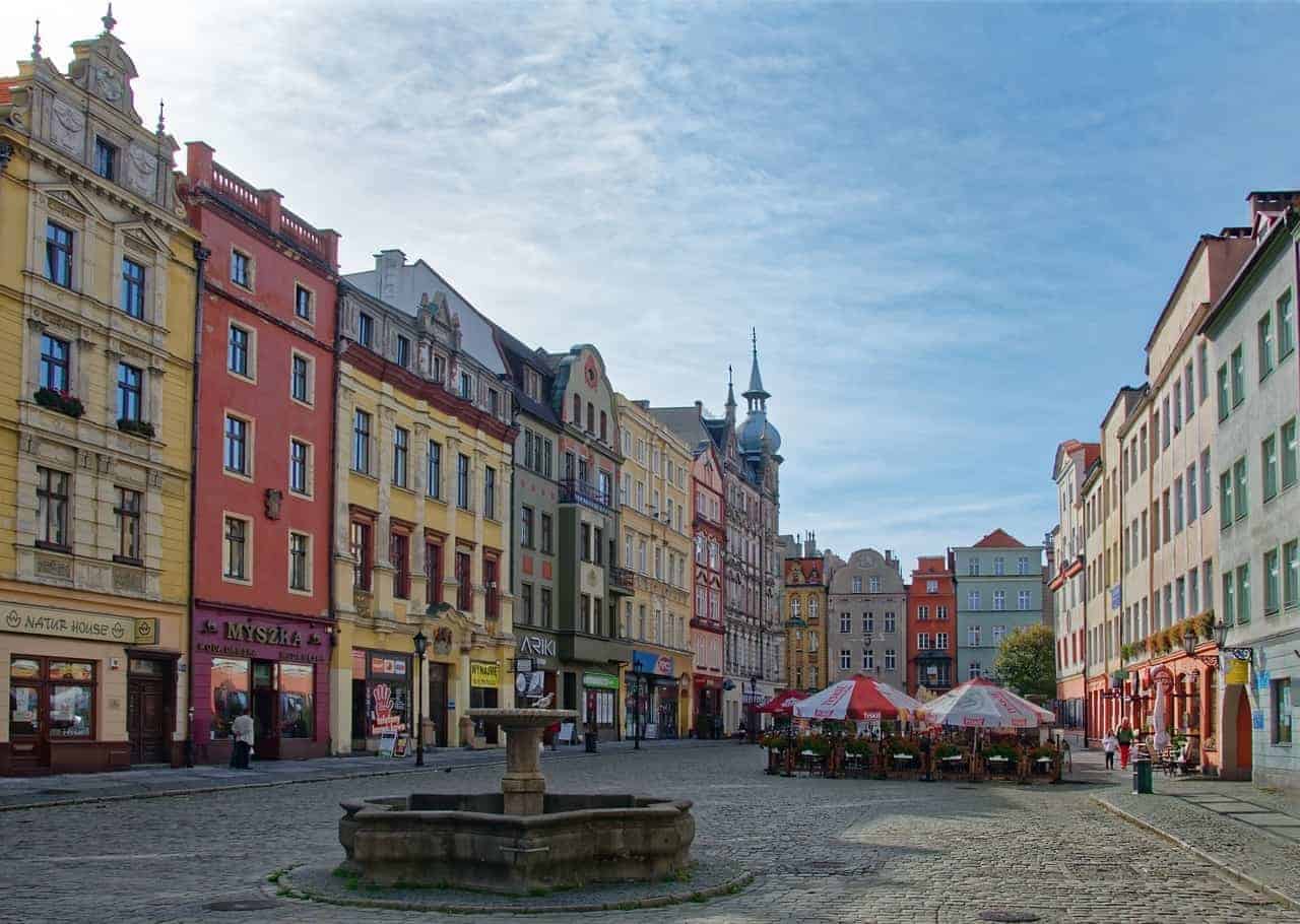 A cobblestone town square in Dolnośląskie, Poland, with colorful historic buildings, a central stone fountain, and outdoor café seating under umbrellas—one of the charming places to visit in the region.