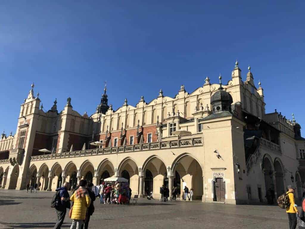 People walk near the historic Cloth Hall building, one of the iconic historical landmarks in Poland, in Krakow’s Main Market Square under a clear blue sky.