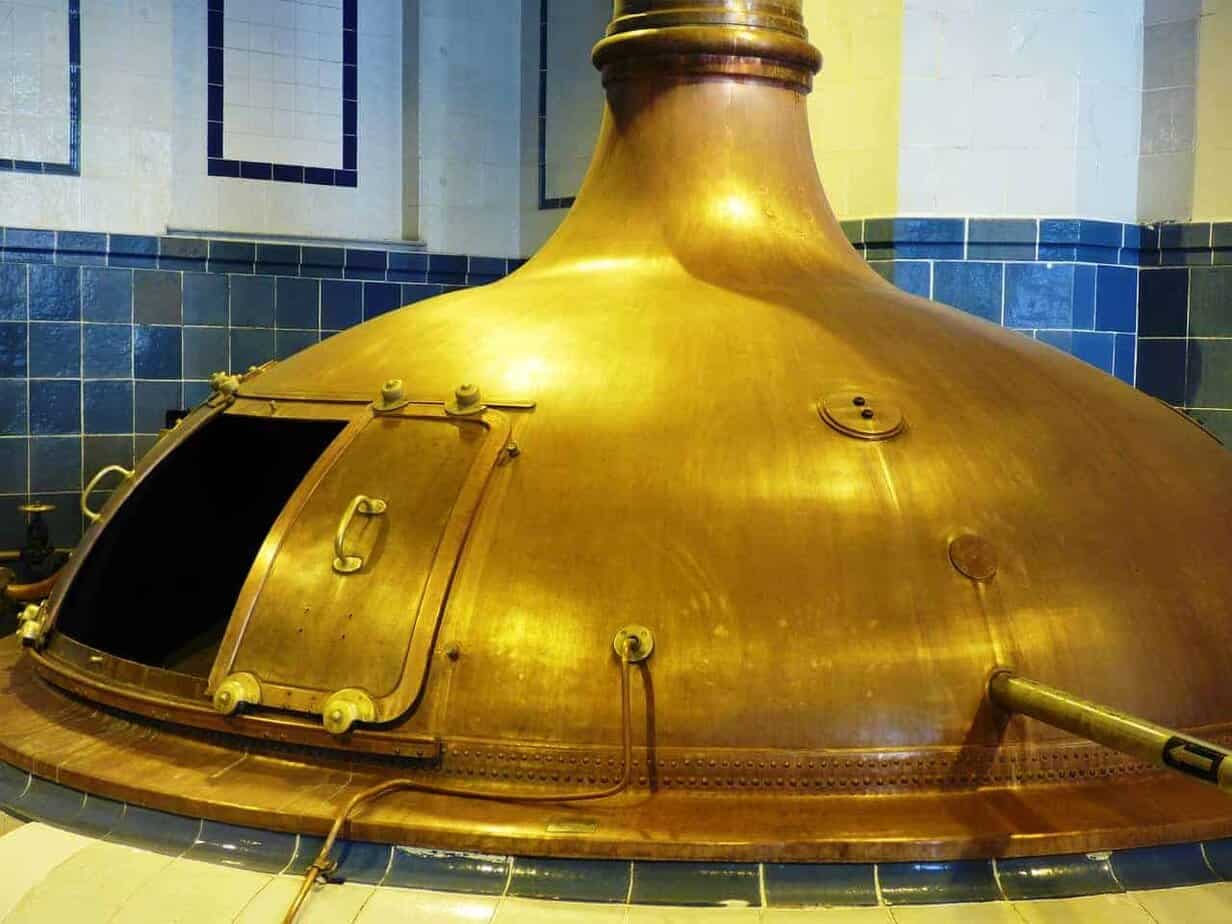 A large copper brewing kettle with an open hatch stands against blue and white tiled walls—a unique sight for those looking to travel and discover the best places to visit in Slaskie, Poland’s rich brewery heritage.