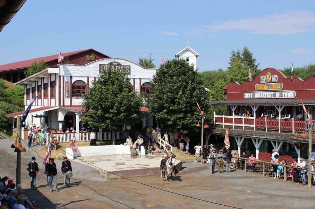 Outdoor Western-themed performance in Slaskie, Poland, with actors in period costumes, horses, and two saloon-style buildings surrounded by trees and spectators—one of the best places for a unique experience.