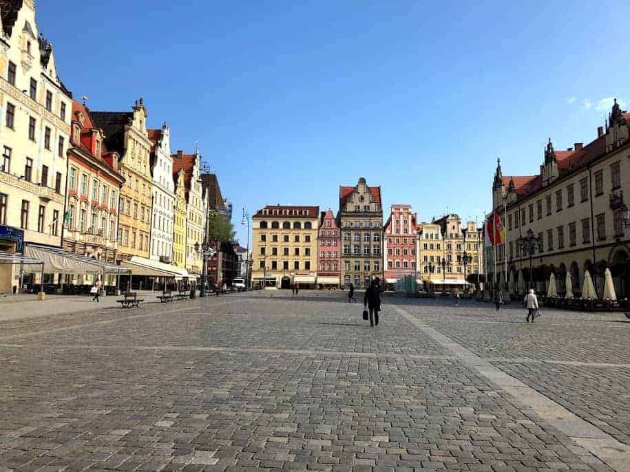 A spacious cobblestone square in Dolnośląskie, Poland, lined with colorful historic buildings under a clear blue sky; a few people walk in the open area—one of the best places to visit.