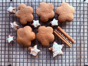 Polish gingerbread cookies and iced star-shaped cookies are arranged on a cooling rack with two cinnamon sticks on a wooden surface.